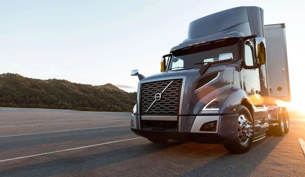 Volvo day cab on the road with sun shining behind it.