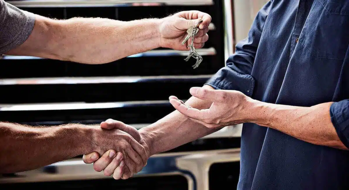 Two people shaking hands and one handing the other a set of keys in front of a truck grille